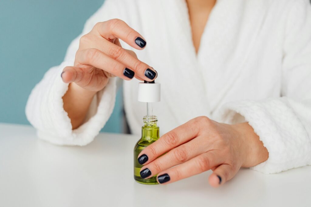 Balmy Herb Close-up of a woman in a white bathrobe using a skincare product dropper with painted nails.
